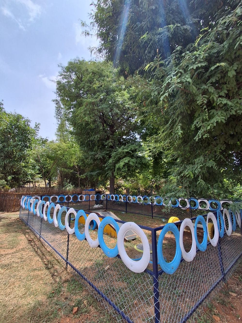 Blue and white tyre hoops mounted vertically along a fence line for leap-through agility training.